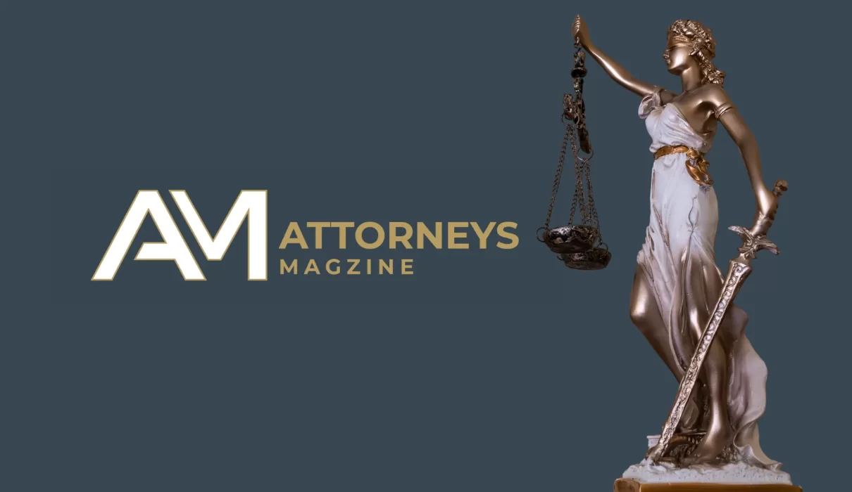 A bronze and white Lady Justice statue holding scales and a sword next to the Attorneys Magazine logo on a dark blue background.