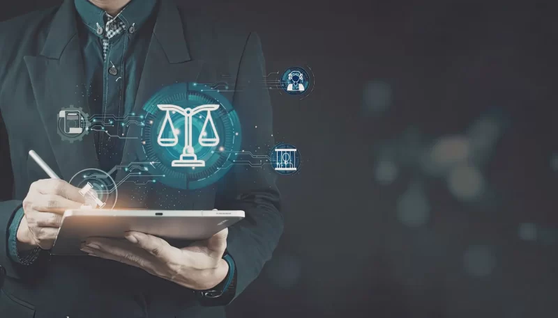 A person in a suit using a stylus on a tablet that displays glowing holographic legal icons, including the scales of justice and a gavel.