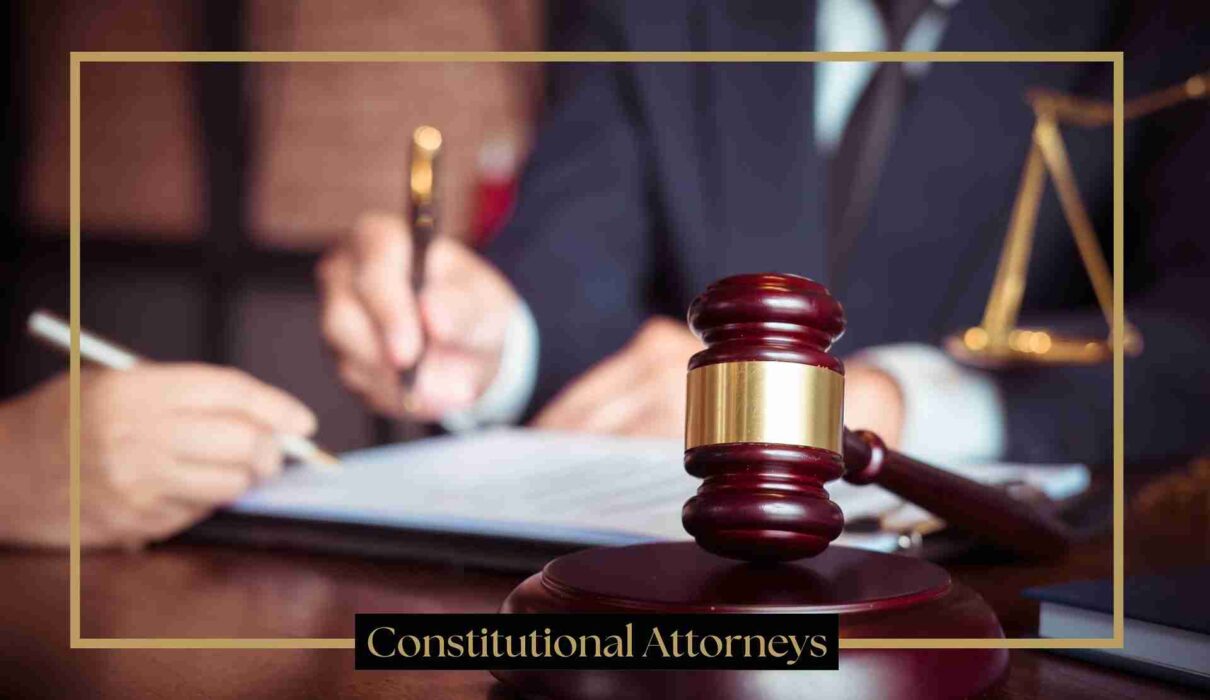 A judge's gavel on a wooden desk in a courtroom setting, with an attorney writing in the background and the text "Constitutional Attorneys" at the bottom.