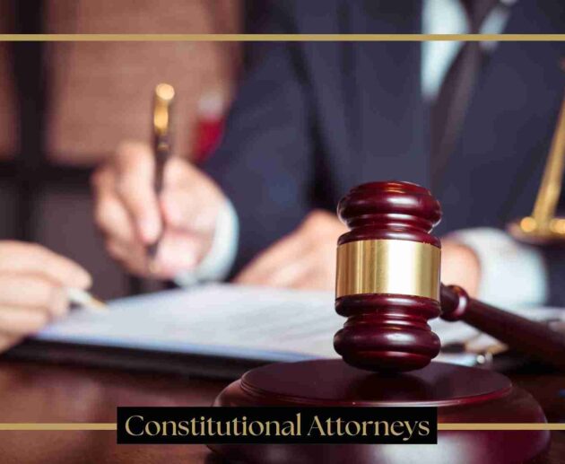 A judge's gavel on a wooden desk in a courtroom setting, with an attorney writing in the background and the text "Constitutional Attorneys" at the bottom.