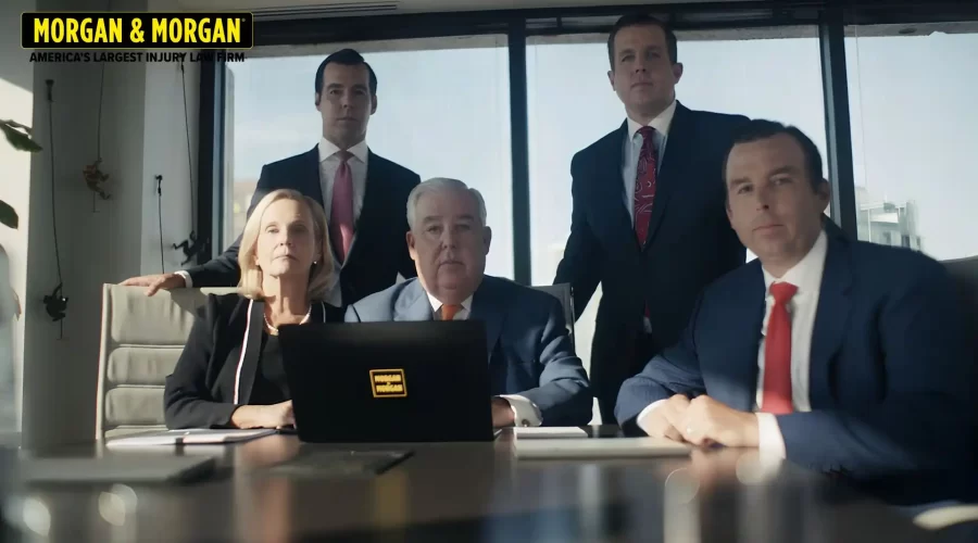 A group portrait of five attorneys from the Morgan & Morgan law firm, including founder John Morgan, seated and standing around a conference table in a modern office.