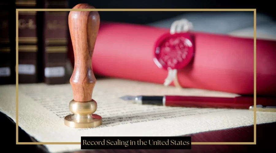 A wooden and brass wax seal stamp stands upright on a piece of parchment paper next to a fountain pen and a rolled red document secured with a red wax seal.