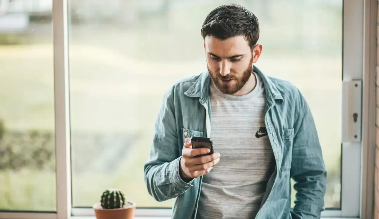 man holding a smartphone near the window -SparkPressFusion